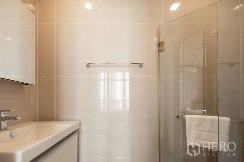 Condominium for rent in Khlong Toei, Bangkok - Main bathroom with vanity sink and a glass-enclosed shower.