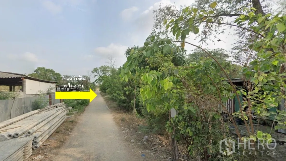 ที่ดิน ขายในThanyaburi, Pathum Thani - ซอยทางเข้าท้องถิ่น สองข้างมีต้นไม้และวัสดุก่อสร้าง มุ่งสู่ช่วงในของแปลง