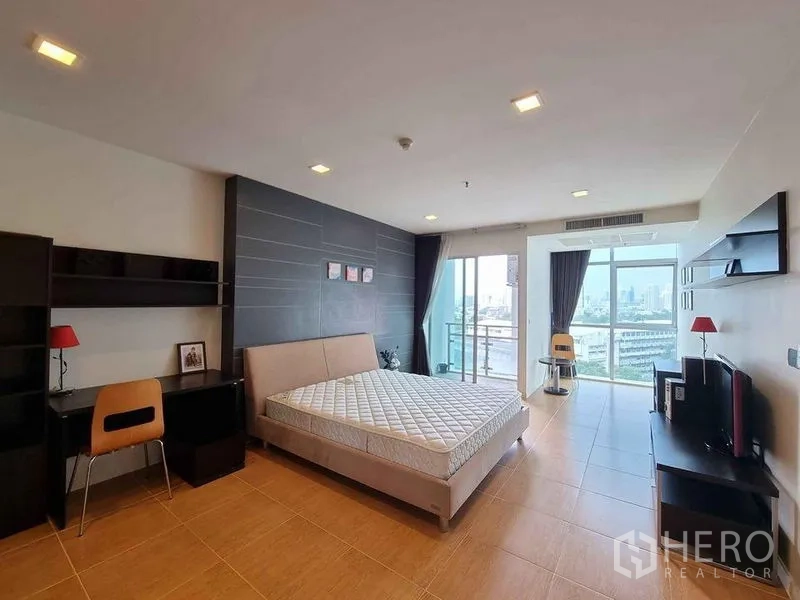 Condominium for rent in Khlong Luang, Pathum Thani - King‑size bedroom with work desk, shelving and two walls of windows facing the skyline.