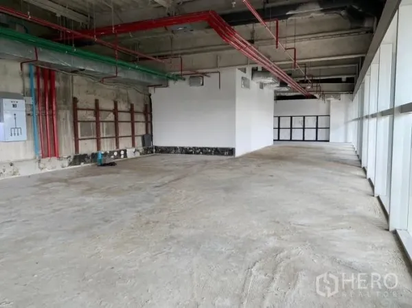 พื้นที่ขายปลีก ให้เช่า - พื้นที่เปล่าทรงยาว มีท่อระบบสีแดงและสีเขียว ตู้ไฟ และผนังกระจกยาวตลอดแนว