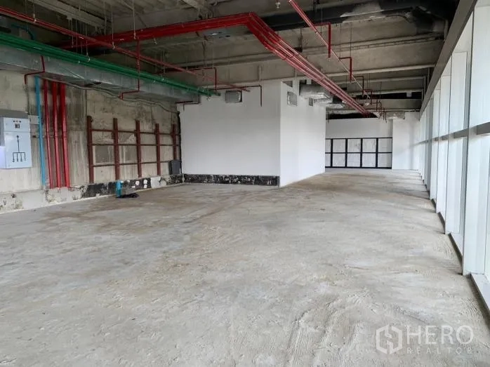 พื้นที่ขายปลีก ให้เช่า - พื้นที่เปล่าทรงยาว มีท่อระบบสีแดงและสีเขียว ตู้ไฟ และผนังกระจกยาวตลอดแนว