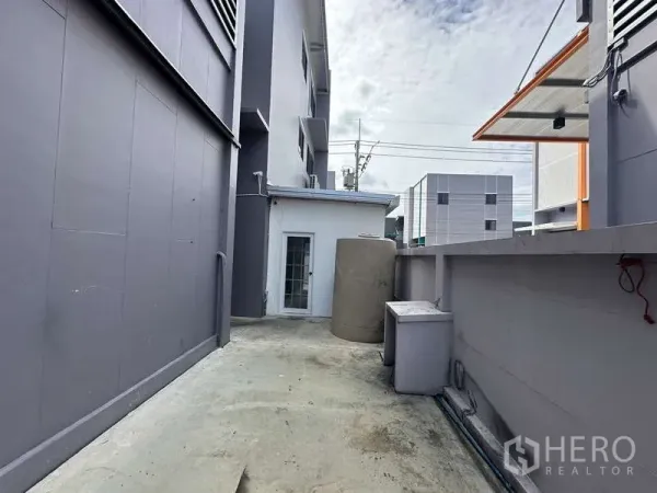 Factory for rent in Lam Luk Ka, Pathum Thani - Service lane along the factory wall with a water tank and utility area.