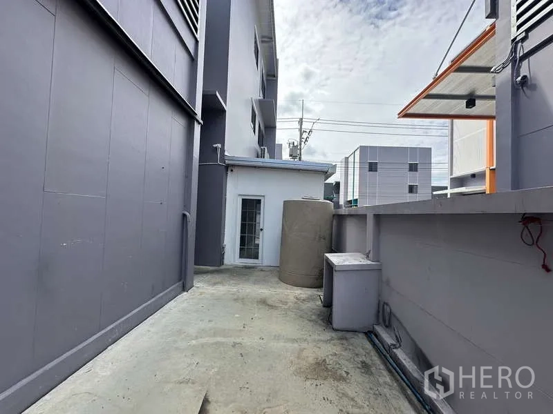 Factory for rent in Lam Luk Ka, Pathum Thani - Service lane along the factory wall with a water tank and utility area.