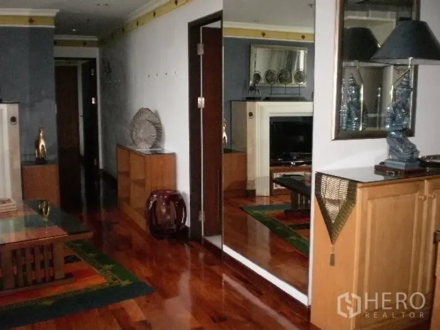 Condominium for rent in Pathum Wan, Bangkok - Hallway with polished wooden floors, a large wall mirror, built-in cabinets and modern decor.