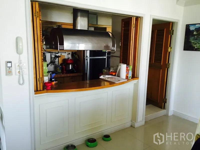 Condominium for rent in Bang Rak, Bangkok - Semi-open kitchen with large stainless extractor hood, wood cabinets and refrigerator.