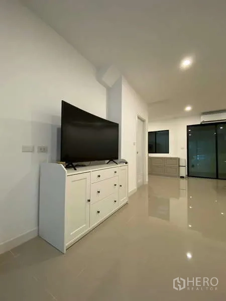 Townhouse for rent in Bang Kapi, Bangkok - Living area with TV console, glossy tile flooring and black-framed sliding door.