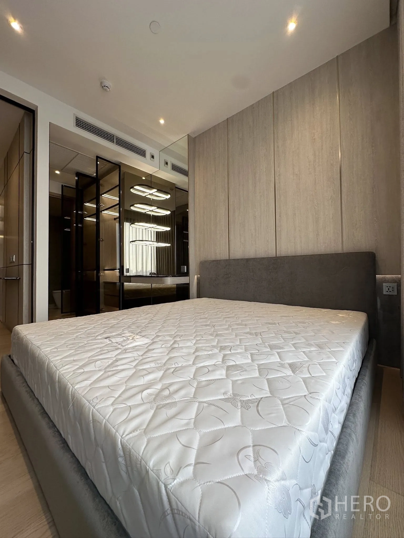 คอนโด for sale in Din Daeng, Bangkok - ห้องนอนมีเตียงบุผ้า ผนังตกแต่ง แผงกระจกเงาตู้เสื้อผ้า และไฟดาวน์ไลท์