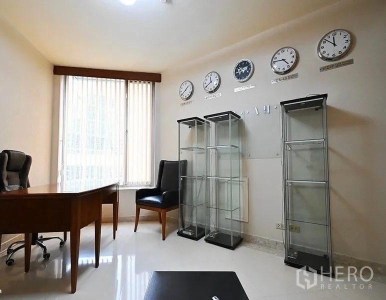 Condominium for rent in Pathum Wan, Bangkok - Home office with desk, leather chair, glass display cabinets, and world clocks on the wall.