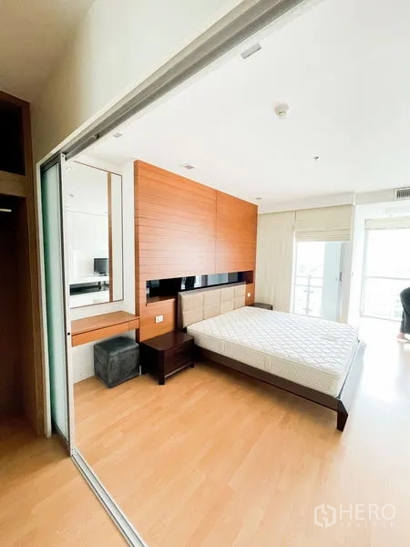 Condominium for rent in Khlong Luang, Pathum Thani - Spacious bedroom featuring a wood headboard, bedside tables, and sliding glass doors to a balcony.