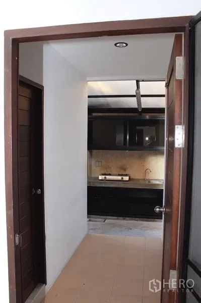 Townhouse for rent in Phaya Thai, Bangkok - Compact kitchen corridor featuring dark cabinetry, gas cooktop, stainless sink, and tiled flooring.