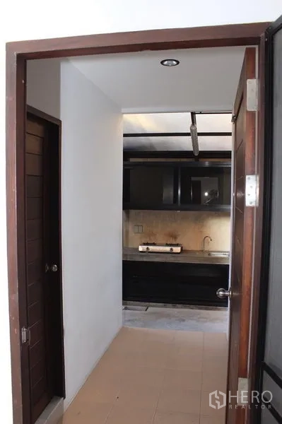 Townhouse for rent in Phaya Thai, Bangkok - Compact kitchen corridor featuring dark cabinetry, gas cooktop, stainless sink, and tiled flooring.