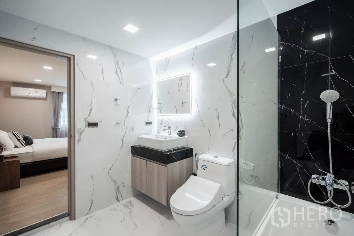 Apartment for rent - Bathroom with illuminated mirror, glass shower enclosure and doorway to the bedroom.