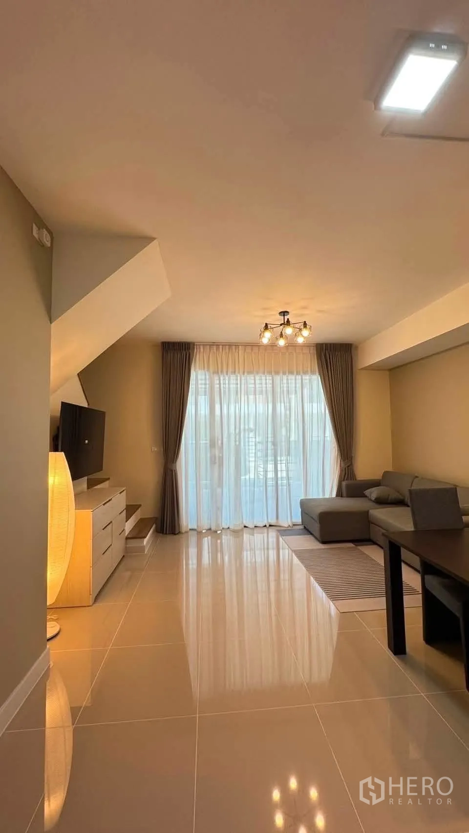 Townhouse for rent in Bang Phli, Samut Prakan - Living room with L-shaped sofa, rug and floor-to-ceiling curtains letting in light.