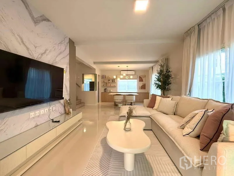 Detached House for rent in Bang Phli, Samut Prakan - Living area with large sofa, marble TV wall and full-height curtains.