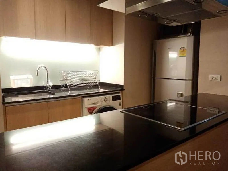 公寓 出租在Sathon, Bangkok - 整体厨房近景，水槽、沥水架、洗烘一体机、电磁炉与不锈钢烟机。