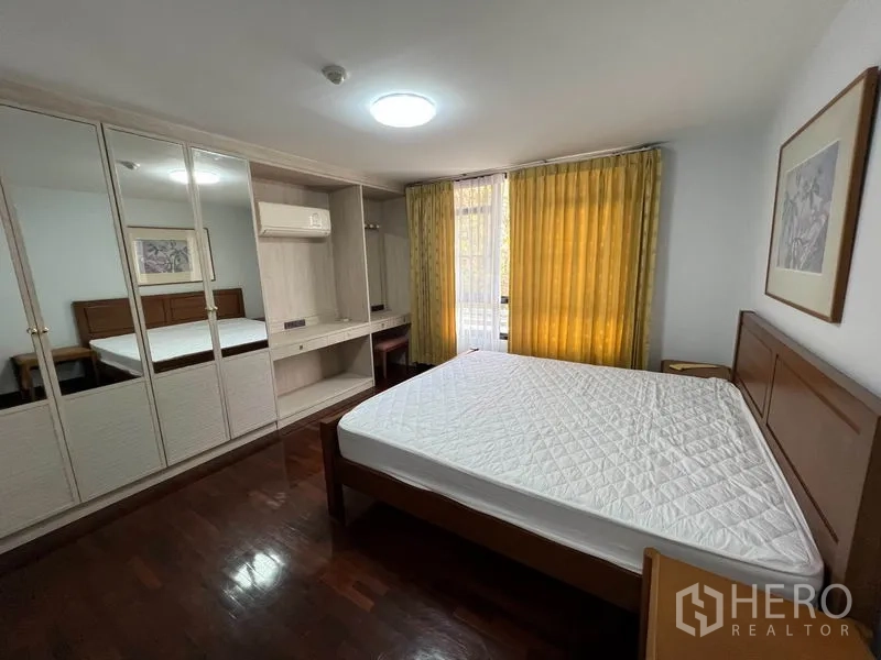 公寓 出租在Watthana, Bangkok - 卧室带镜面衣柜、木床、黄色窗帘与工作区。