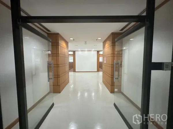 办公空间 出租在Phaya Thai, Bangkok - 穿过玻璃门进入木饰面走廊，照明充足的办公入口。