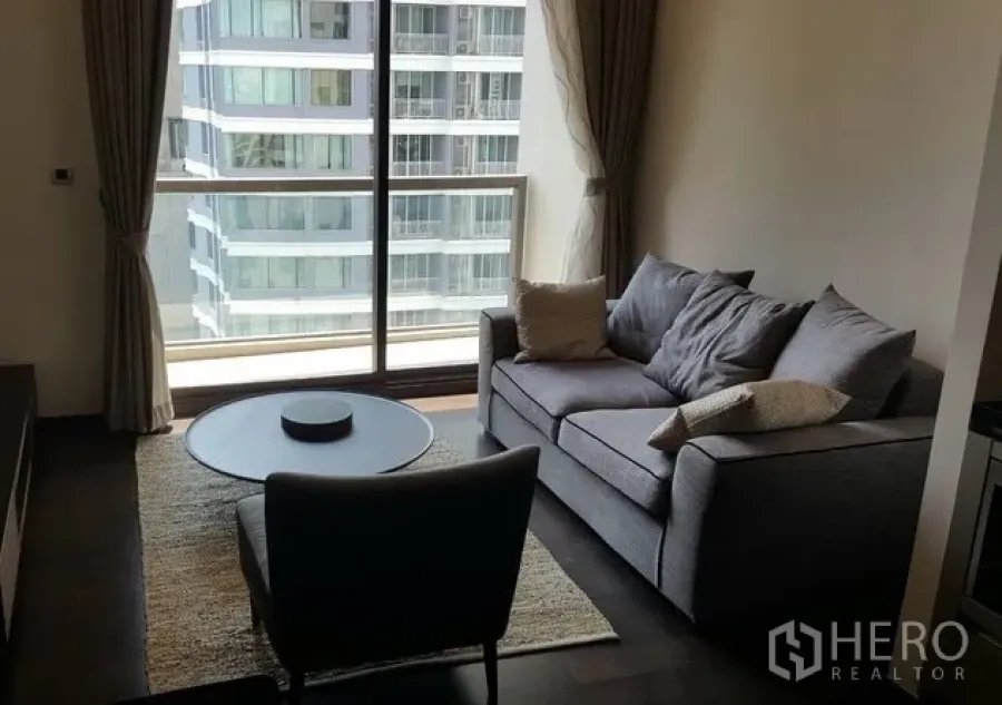 คอนโด ให้เช่าหรือขายในWatthana, Bangkok - ห้องนั่งเล่นสว่างพร้อมหน้าต่างสูงจรดเพดาน โซฟาสีเทา และวิวเมืองในคอนโดโมเดิร์น