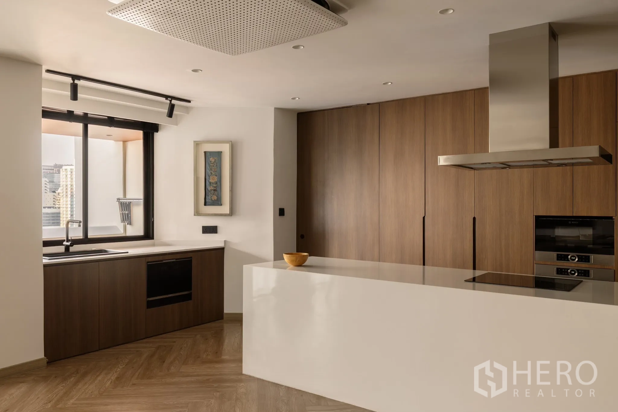 Condominium for sale in Khlong Toei, Bangkok - Modern kitchen with large white island, wood cabinets, window city view, induction hob and stainless range hood.