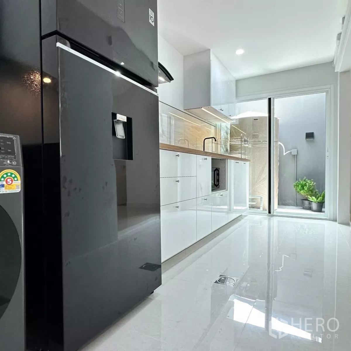 Townhouse for rent in Bang Phli, Samut Prakan - Kitchen close-up showing black fridge, range hood, washer-dryer, microwave and double sink.