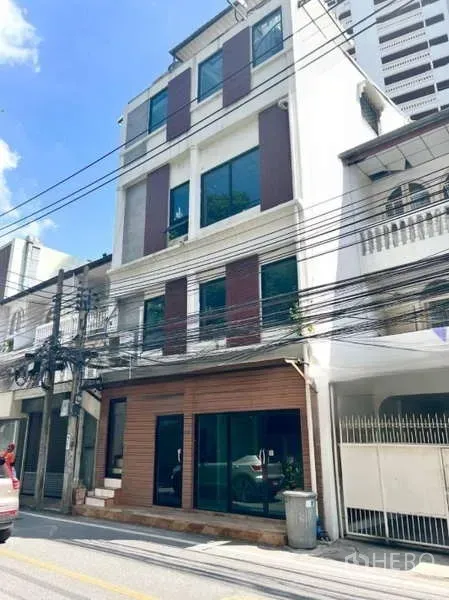 零售空间 出租在Watthana, Bangkok - 四层临街店屋外观，一层玻璃店面，位于曼谷社区，蓝天晴朗。