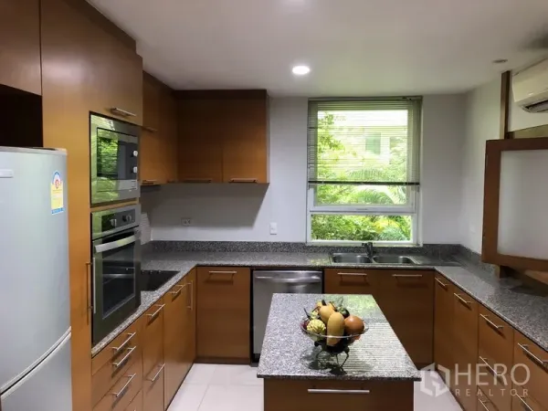 Detached House for rent in Watthana, Bangkok - U-shaped kitchen with granite countertops, built-in oven and a window overlooking greenery.