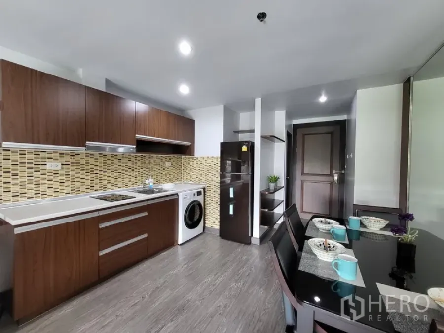 Condominium for rent in Phra Khanong, Bangkok - Modern kitchen with electric cooktop, fridge, washer, and a set dining table.
