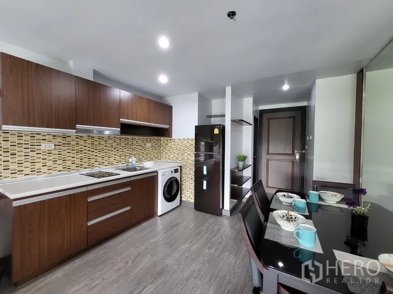 Condominium for rent in Phra Khanong, Bangkok - Modern kitchen with electric cooktop, fridge, washer, and a set dining table.