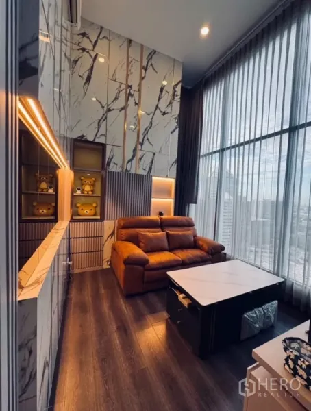 Condominium for rent in Chatuchak, Bangkok - Cozy living area with marble accent wall, feature lighting, and floor-to-ceiling windows.