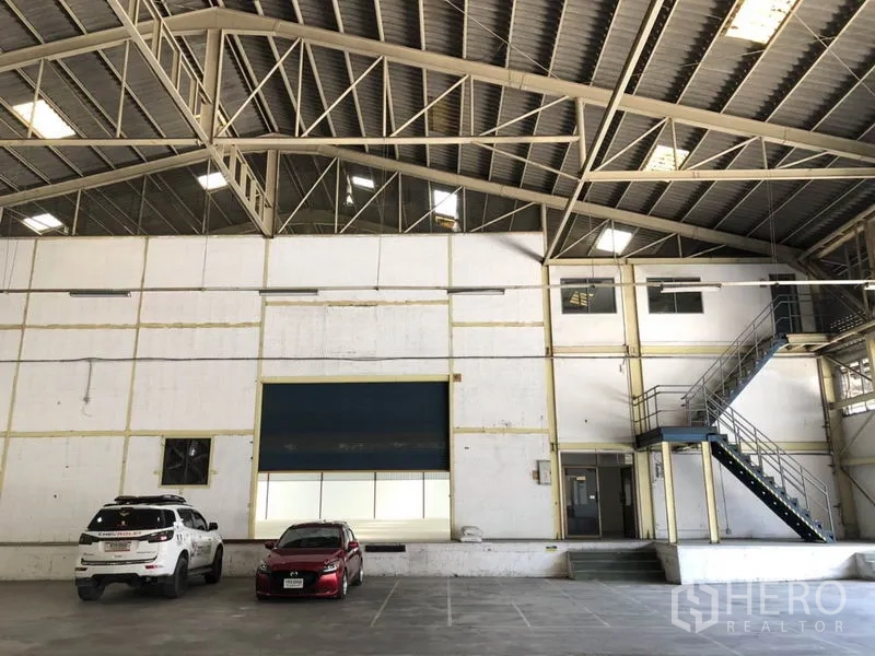 คลังสินค้า ให้เช่าในMueang Samut Prakan, Samut Prakan - ผนังด้านหน้าโกดังมีประตูม้วนขนาดใหญ่และบันไดใต้โครงหลังคาเหล็ก.