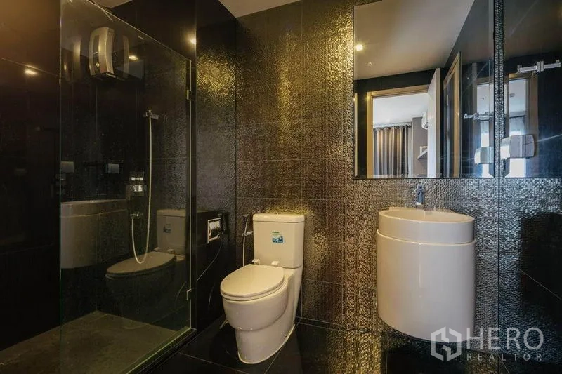 公寓 出租或出售在Khlong Toei, Bangkok - 现代卫浴，玻璃淋浴间、深色纹理墙砖、圆形台盆与马桶。
