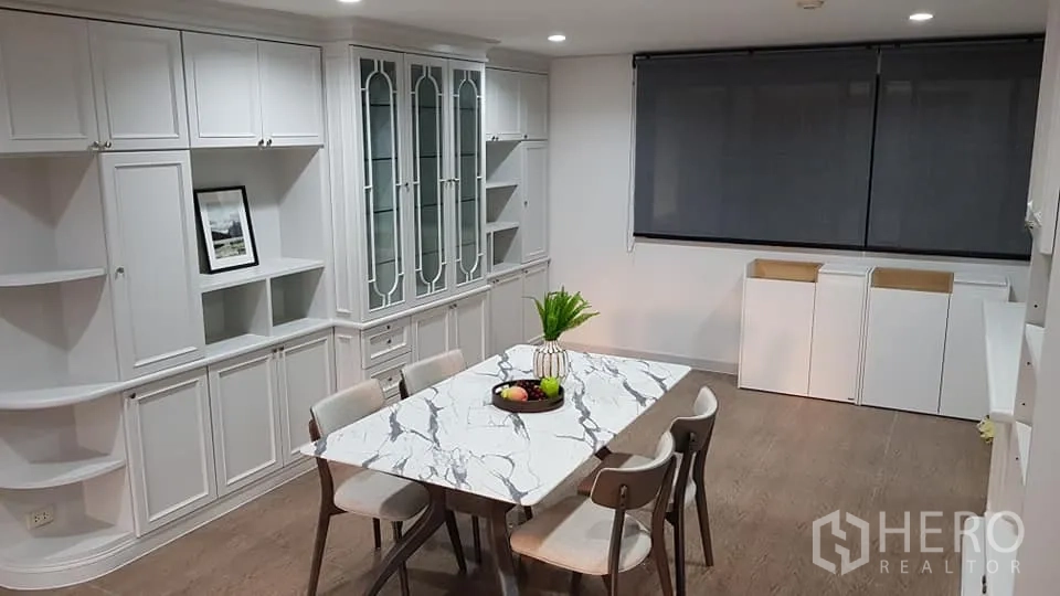 公寓 for rent in Bang Rak, Bangkok - 餐厅配大理石纹餐桌与四把椅子，整面白色壁柜带玻璃展示门，木地板与带卷帘的大窗。