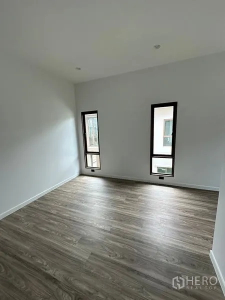 Detached House for rent in Bang Kapi, Bangkok - Secondary bedroom with two slim vertical windows and laminate floors.