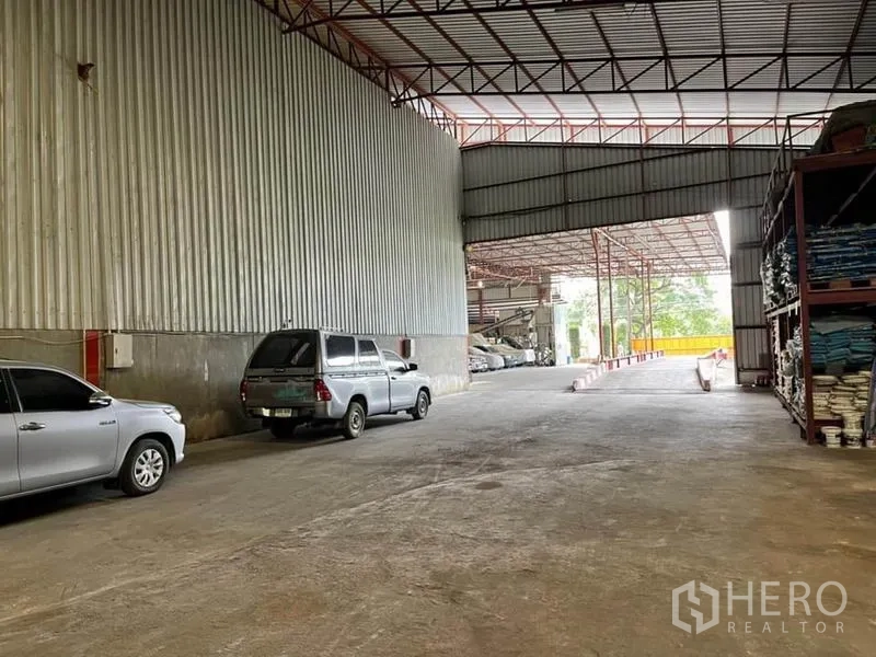 货栈 出售在Lam Luk Ka, Pathum Thani - 室内通道通向院区，右侧为货架，墙边停有车辆。