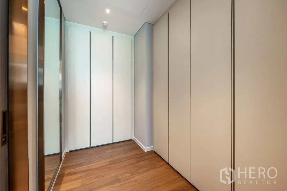 Condominium for rent or sale in Pathum Wan, Bangkok - Corridor with built-in wardrobes and wooden flooring leading to bedroom.
