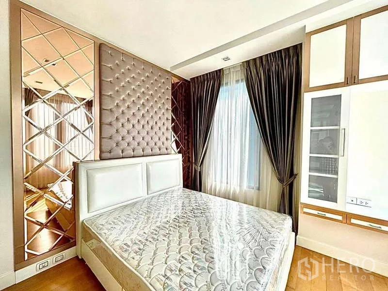 Condominium for rent in Bangkok - Sunlit bedroom featuring padded headboard, mirrored panels and wood flooring.