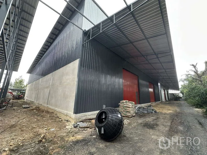 Warehouse for rent in Lam Luk Ka, Pathum Thani - Side view of the warehouse with red roller doors, metal cladding and extended roof awning.