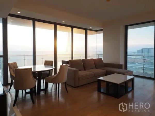 Condominium for rent in Yan Nawa, Bangkok - Bright lounge and dining beside wraparound glass, opening to balcony at sunset.