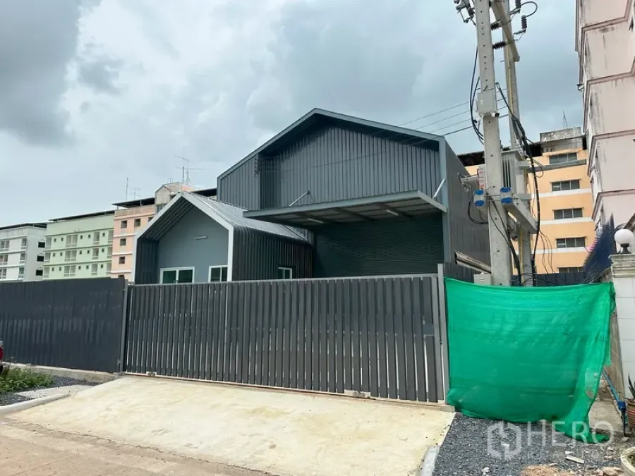 Factory for rent in Khlong Luang, Pathum Thani - Modern gated factory exterior with grey metal cladding and high fence in an urban setting.