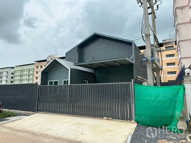 Factory for rent in Khlong Luang, Pathum Thani - Modern gated factory exterior with grey metal cladding and high fence in an urban setting.