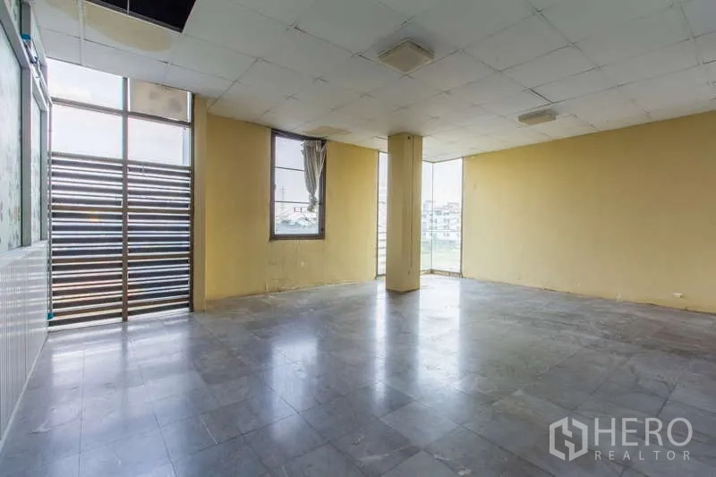 办公空间 出租或出售在Huai Khwang, Bangkok - 开放房间，黄色墙面，带窗户和金属百叶门通往阳台。