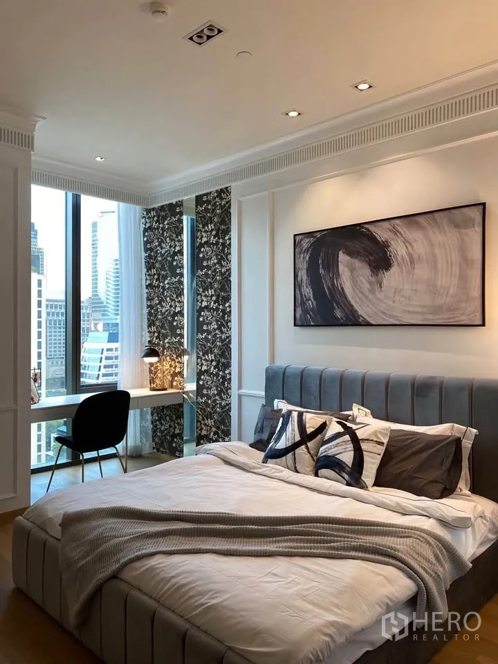 Condominium for rent in Pathum Wan, Bangkok - Bedroom with upholstered bed, abstract artwork, window-side desk, and patterned wall panels.