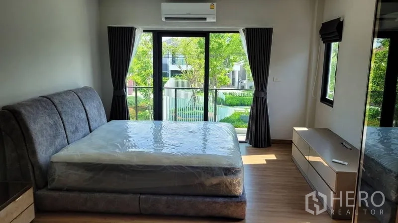 Detached House for rent in Don Mueang, Bangkok - Master bedroom with glass doors to balcony, garden view and wood floors.