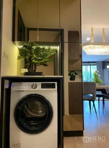 คอนโด ให้เช่าในPathum Wan, Bangkok - เครื่องซักผ้าแบบฝาหน้าในตู้บิวท์อิน หน้าบานกระจก มองเห็นโคมระย้าบริเวณทานอาหาร