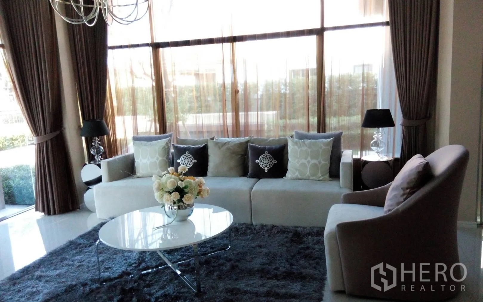 Detached House for rent or sale in Prawet, Bangkok - Bright living room with floor-to-ceiling windows, sectional sofa, lamps and plush rug.