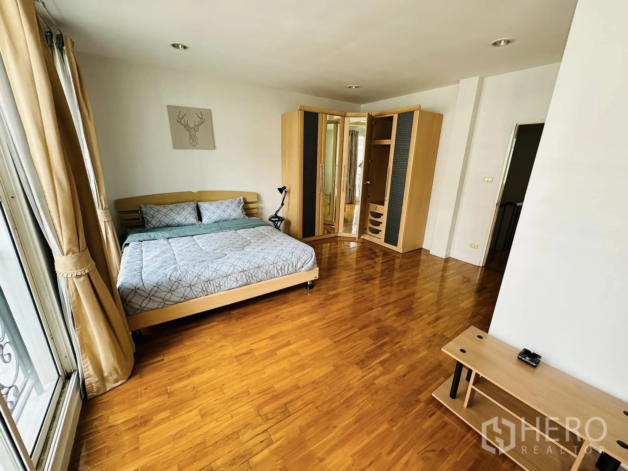 Townhouse for rent in Watthana, Bangkok - Master bedroom with wood floors, large windows and a mirrored corner wardrobe.