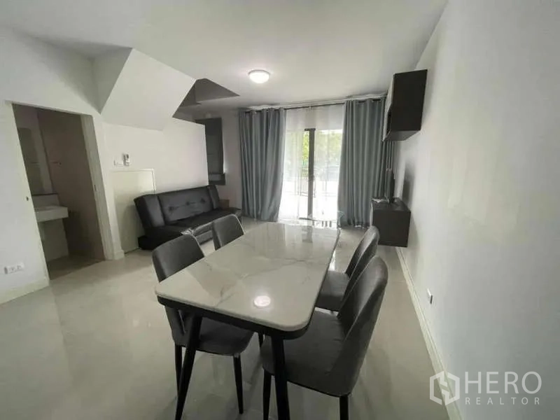 Townhouse for rent or sale in Phasi Charoen, Bangkok - Open-plan dining and living room with marble-top table, sofa and sliding doors.