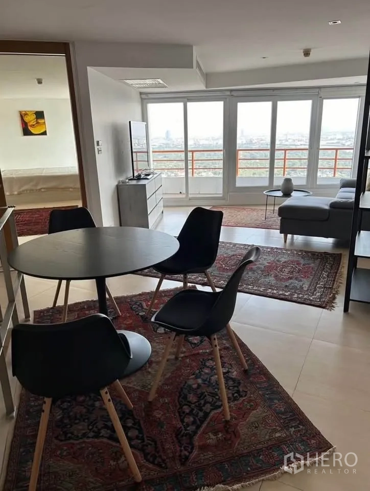 Condominium for rent or sale in Yan Nawa, Bangkok - Dining nook with round black table, open-plan lounge and full-width balcony windows.