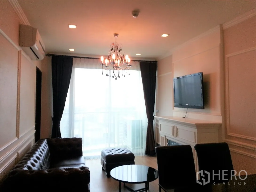 คอนโด ให้เช่าหรือขายในWatthana, Bangkok - ห้องนั่งเล่นสไตล์หรู โคมระย้า โซฟาหนัง ทีวีติดผนัง และหน้าต่างสูงจรดเพดานเปิดสู่ระเบียงวิวเมือง