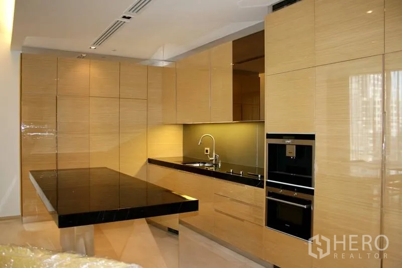 公寓 出租在Bang Rak, Bangkok - 现代L型厨房，亮木柜体与黑色石面岛台，内置烤箱与灯带。